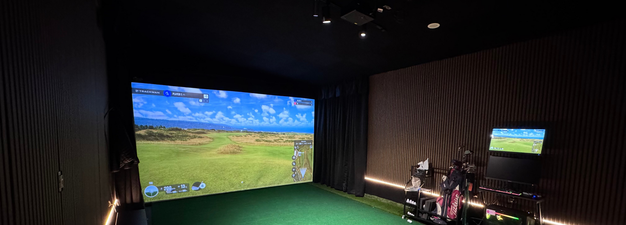 Indoor golf simulator room with large screen displaying a golf course.
